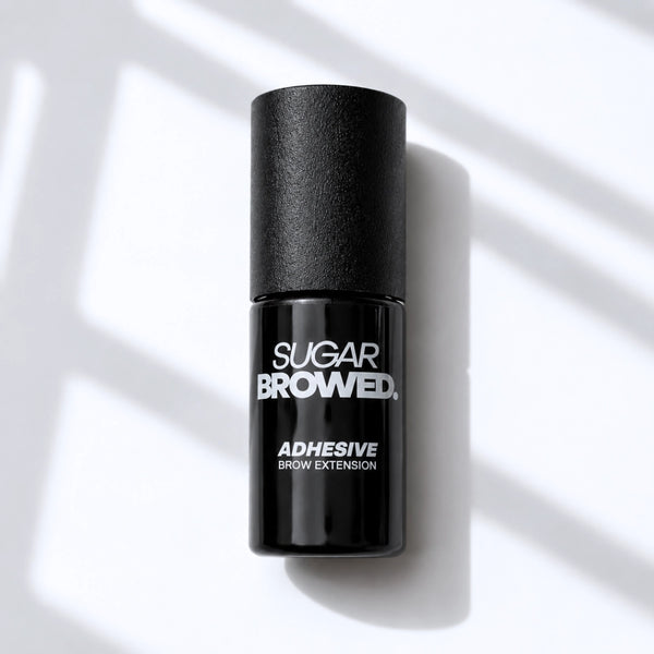 Black bottle of SUGAR BROWED. Adhesive for brow extensions on clean studio background – professional eyebrow glue for long-lasting results