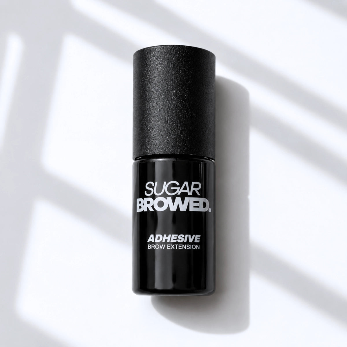 Black bottle of SUGAR BROWED. Adhesive for brow extensions on clean studio background – professional eyebrow glue for long-lasting results